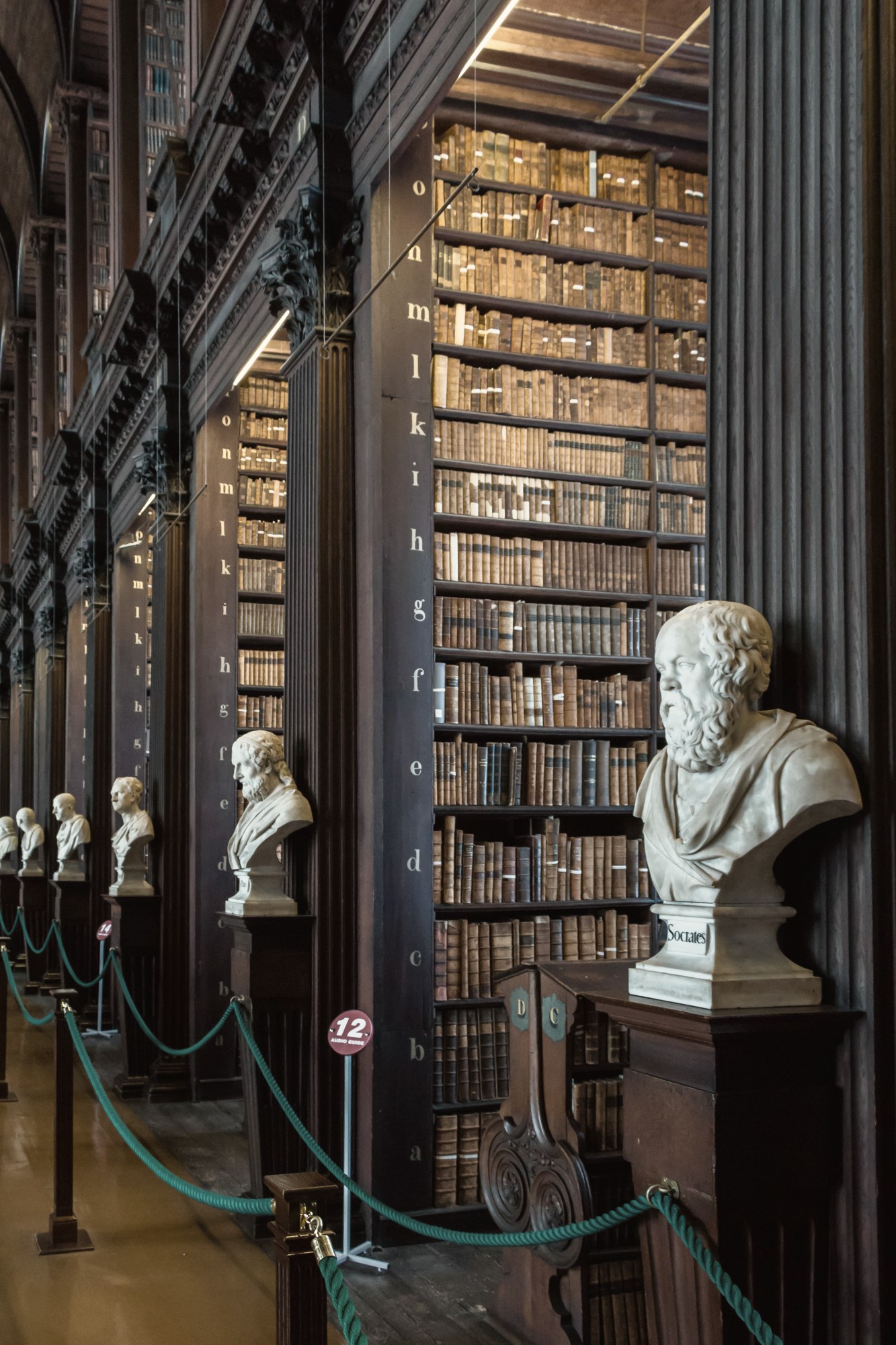 A long library hall at night, shelves rising to a vaulted ceiling